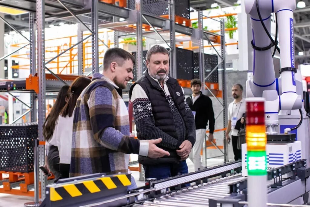 Mitarbeiter beobachten automatisiertes Förderbandsystem in einem Lager mit Kartons und moderner Technik.