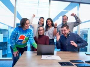 Gruppe von Männern und Frauen an einem Tisch schaut gemeinsam auf einen Laptop während eines Teammeetings im Büro.