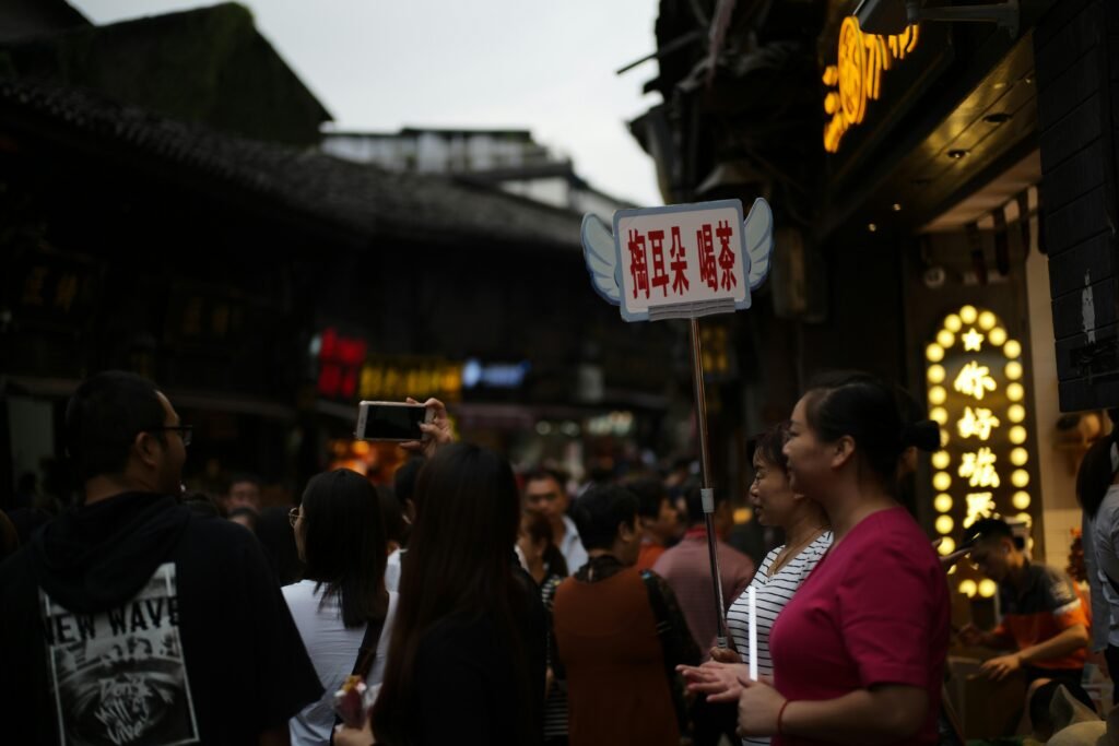 Personen gehen in der abendlichen Dämmerung auf einer geschäftigen Straße mit modernen Gebäuden im Hintergrund.