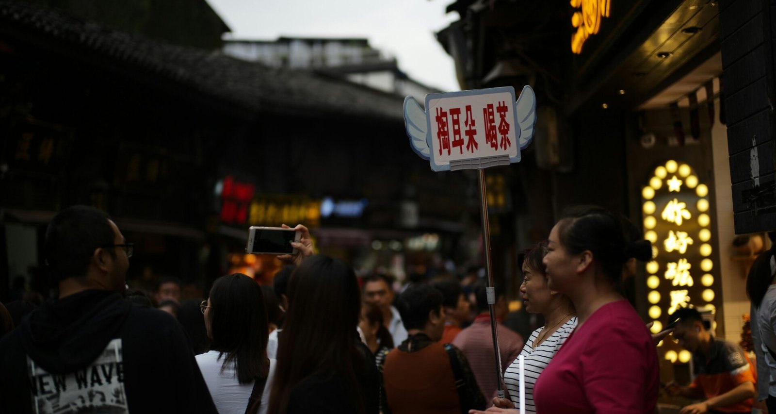 Menschen schlendern bei Dämmerung über eine gut besuchte Straße in der Innenstadt mit leuchtenden Schaufenstern.