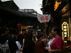 Menschen schlendern bei Dämmerung über eine gut besuchte Straße in der Innenstadt mit leuchtenden Schaufenstern.
