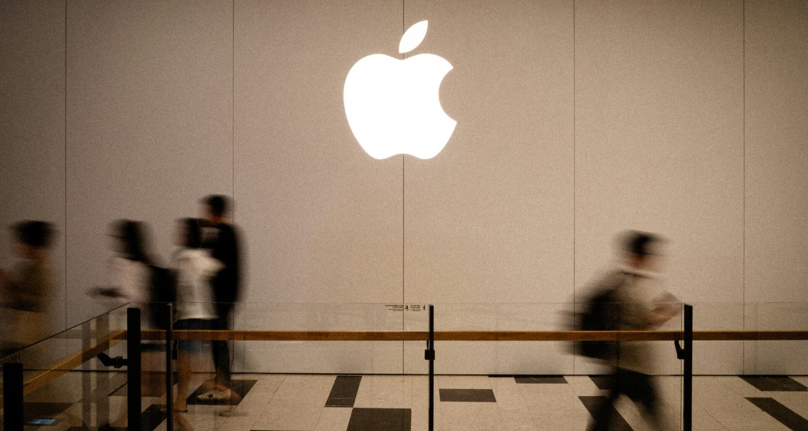 Mehrere Personen laufen an einem großen, beleuchteten Apple-Logo entlang in einer städtischen Umgebung.