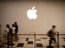 Mehrere Personen laufen an einem großen, beleuchteten Apple-Logo entlang in einer städtischen Umgebung.