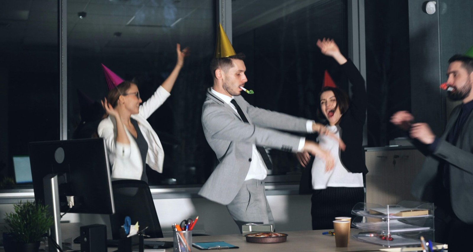 Mitarbeiter mit Partyhüten tanzen im modernen Büro während einer gemeinsamen Firmenfeier