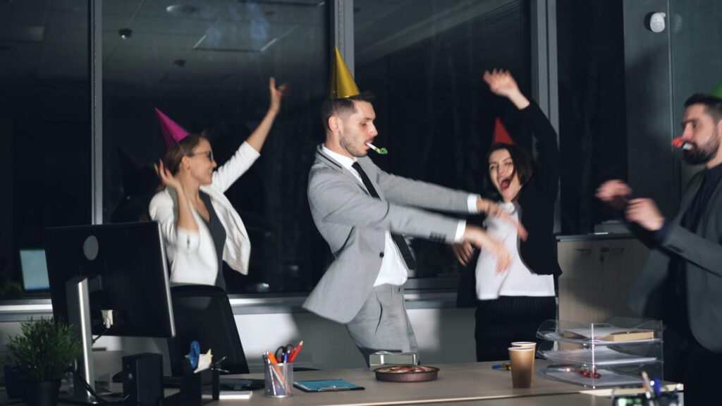 Menschen mit Partyhüten tanzen gemeinsam bei einer Feier im Büro mit moderner Einrichtung und festlicher Stimmung.