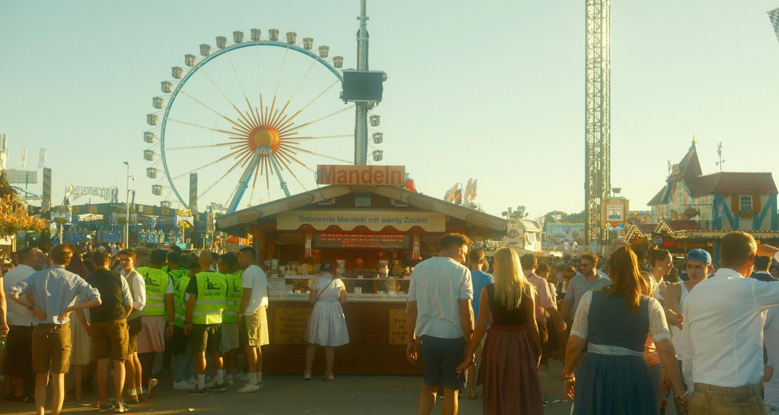 Große Menschenmenge bei sonnigem Wetter vor einem Riesenrad in einem Freizeitpark