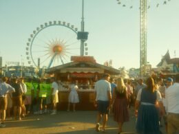 Große Menschenmenge bei sonnigem Wetter vor einem Riesenrad in einem Freizeitpark