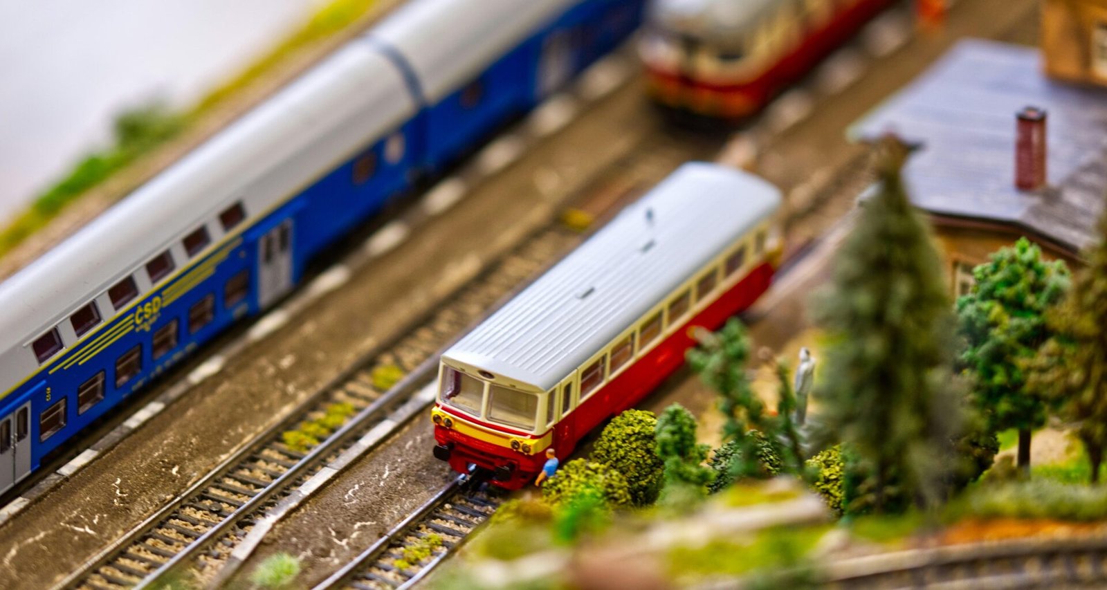 Miniaturzug mit mehreren Wagen fährt auf Modellgleisen – Modellbahnanlage mit detailreich gestalteten Zügen