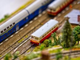 Miniaturzug mit mehreren Wagen fährt auf detailreichen Modelleisenbahn-Gleisen, aus der Vogelperspektive aufgenommen.