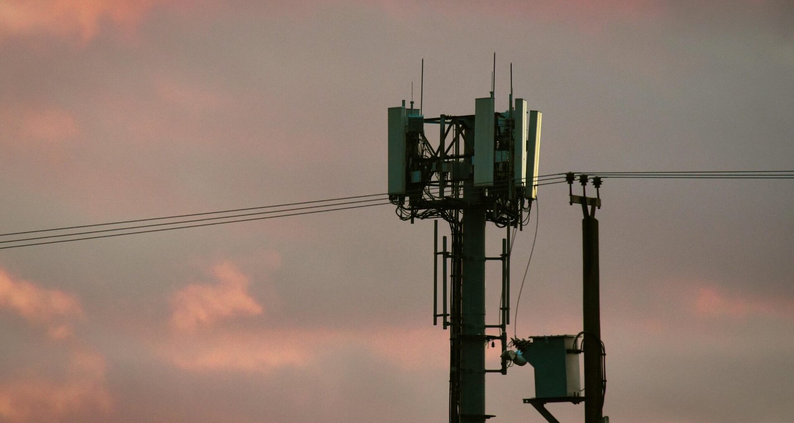 Ein Mobilfunkmast steht silhouettenhaft vor einem bunten, abendlichen Himmel im Sonnenuntergang.