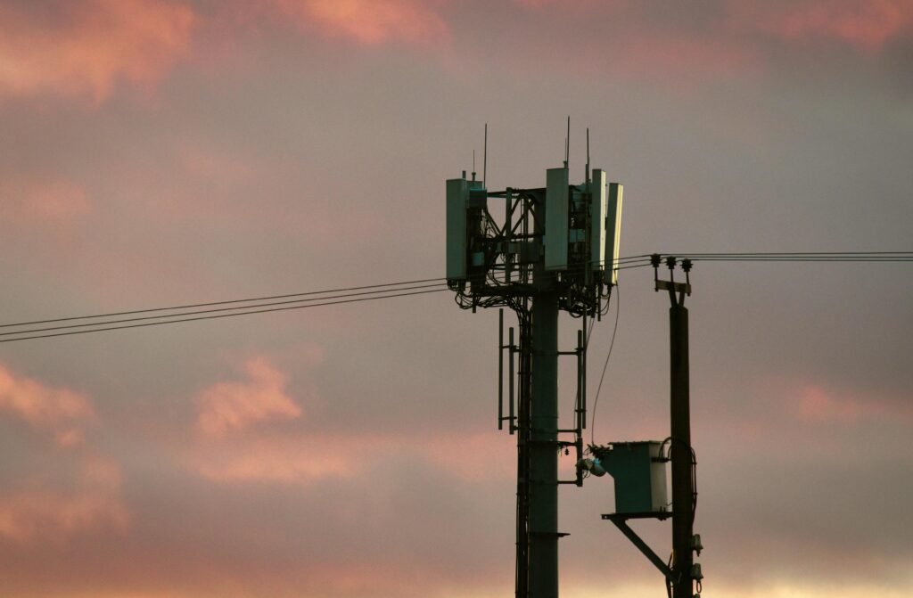 Ein Mobilfunkmast steht silhouettenhaft vor einem farbigen Sonnenuntergangshimmel mit lebhaften Wolken.