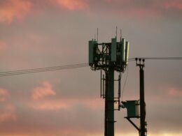 Ein Mobilfunkmast steht silhouettenhaft vor einem farbigen Sonnenuntergangshimmel mit lebhaften Wolken.