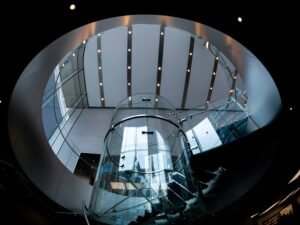 Ein Glasaufzug wird von modernen architektonischen Strukturen eingerahmt und steht im Zentrum des Bauwerks.