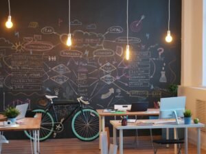 Modernes Büro mit Kreidetafelwand, Arbeitsplatz und an der Wand abgestellten Fahrrädern in einem offenen Raum