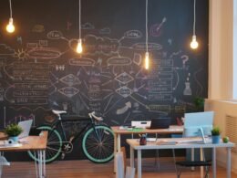 Modern eingerichtetes Büro mit einer schwarzen Tafelfläche an der Wand und abgestellten Fahrrädern im Raum.