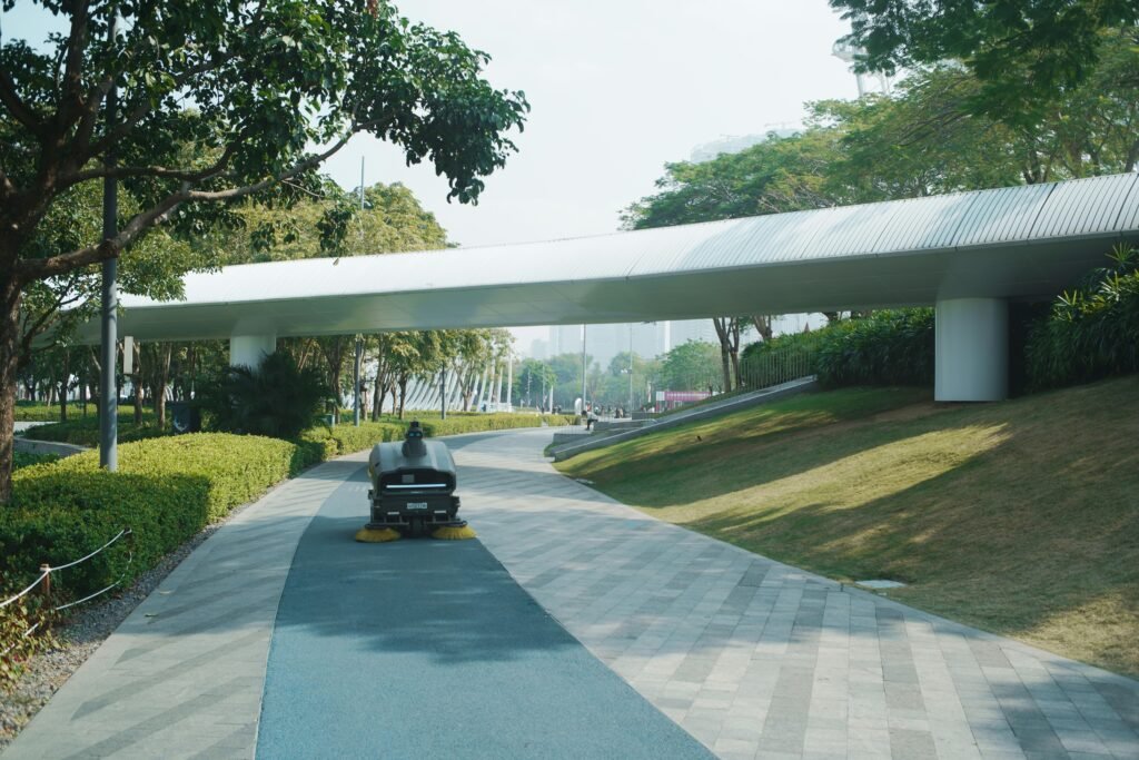 Moderne Fußgängerbrücke aus Metall über einen bepflanzten Parkweg mit zeitgenössischer Architektur im Fokus