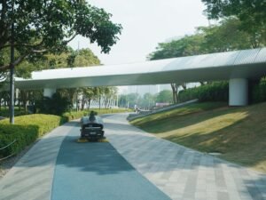 Moderne Fußgängerbrücke aus Metall über einen bepflanzten Parkweg mit zeitgenössischer Architektur im Fokus