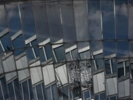 Eine moderne Fassadenansicht eines Gebäudes mit Glasfront und markanten Reflexionen städtischer Umgebung