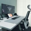 Moderner Schreibtisch mit Computer, ergonomischem Stuhl und minimalistischer Ausstattung in einem hellen Büro.
