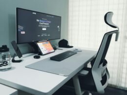 Moderner Schreibtisch mit Computer, ergonomischem Stuhl und minimalistischer Ausstattung in einem hellen Büro.