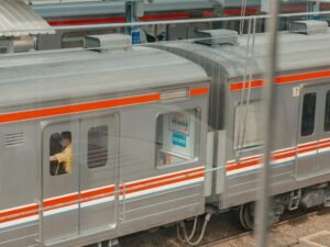 Moderner silberner Zug mit orangefarbener Linie steht am Bahnsteig einer Bahnhofsstation, aufgenommen von Reyhan Aviseno.