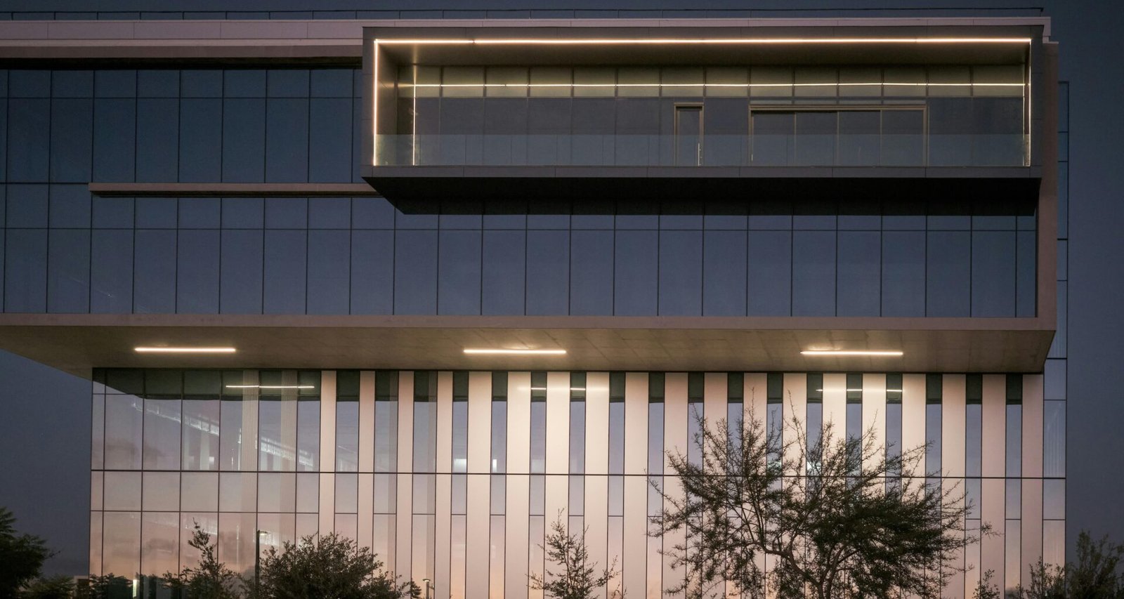 Außenansicht eines modernen Bürogebäudes bei Dämmerung mit leuchtenden Fenstern, zeitgemäße Architektur im urbanen Umfeld