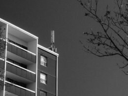 Modernes Apartmentgebäude mit mehreren Balkonen und kahlen Bäumen im Vordergrund, fotografiert bei Tageslicht.