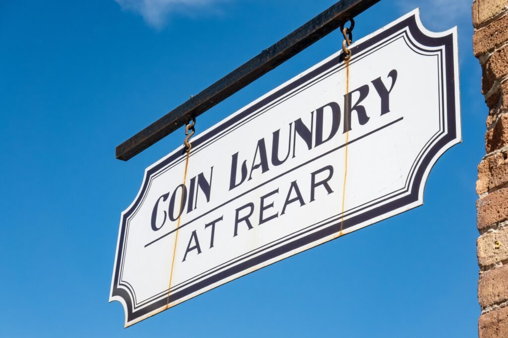 Coin Laundry Schild hängt an einer Gebäudeecke vor blauem Himmel und steht für moderne Selbstbedienungs-Waschsalons.