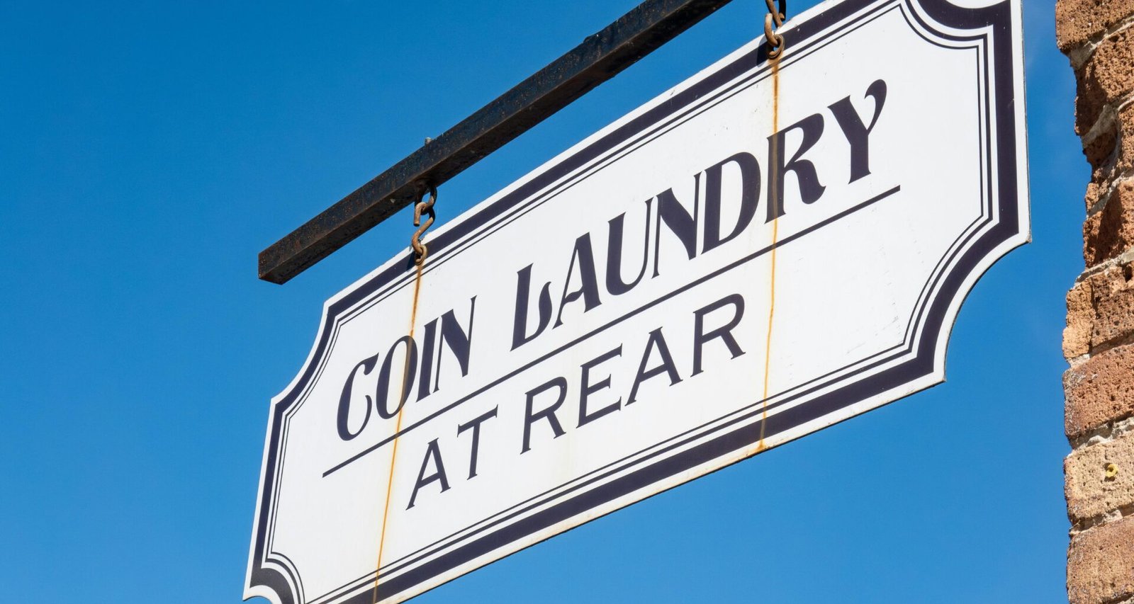 Coin Laundry Schild hängt an einer Gebäudeecke vor blauem Himmel und steht für moderne Selbstbedienungs-Waschsalons.