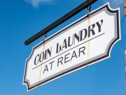 Coin Laundry Schild hängt an einer Gebäudeecke vor blauem Himmel und steht für moderne Selbstbedienungs-Waschsalons.