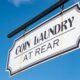 Coin Laundry Schild hängt an einer Gebäudeecke vor blauem Himmel und steht für moderne Selbstbedienungs-Waschsalons.