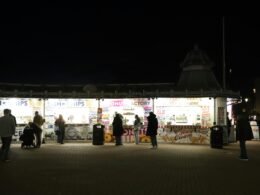 Menschen stehen und schlendern an beleuchteten Essensständen in der Nacht auf einem belebten Markt