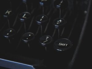 Nahaufnahme von schwarzen Vintage-Schreibmaschinentasten vor dunklem Hintergrund, Fokus auf Details der Typenmechanik.