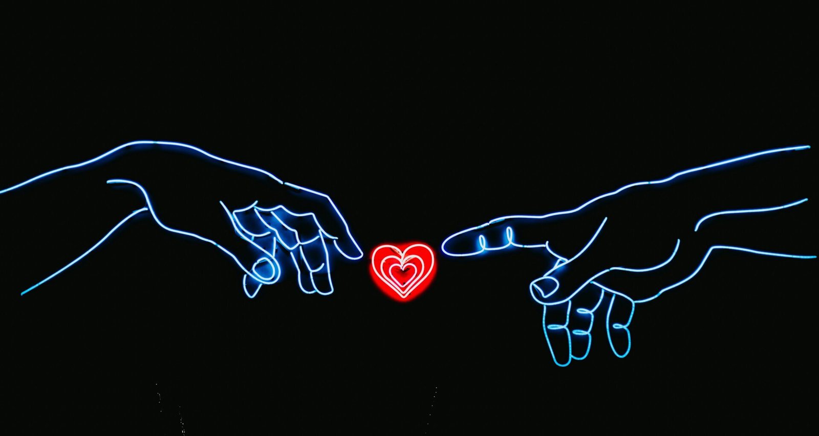 Zwei Hände nähern sich einem herzförmigen Neonlicht auf dunklem Hintergrund, rote und blaue Farbakzente erleuchten das Bild.