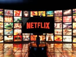 Das Netflix Logo ist auf einem Bildschirm mit mehreren Filmplakaten im Hintergrund zu sehen.