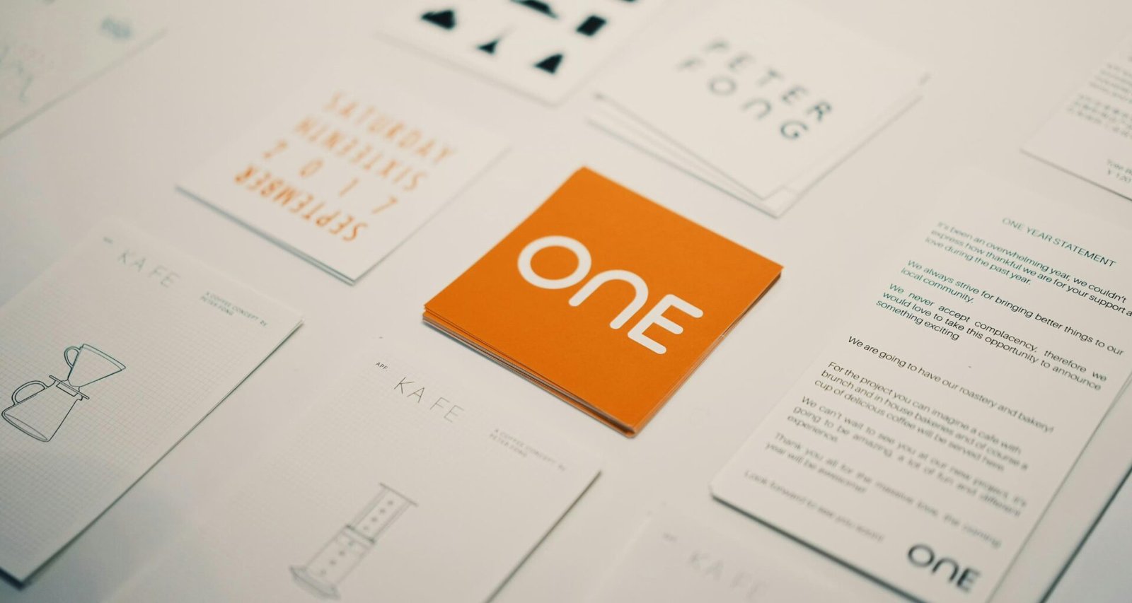 Orange Karte mit "one"-Logo im Zentrum mehrerer anderer Spiel- oder Visitenkarten auf hellem Untergrund