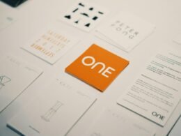 Orange Karte mit "one"-Logo im Zentrum mehrerer anderer Spiel- oder Visitenkarten auf hellem Untergrund