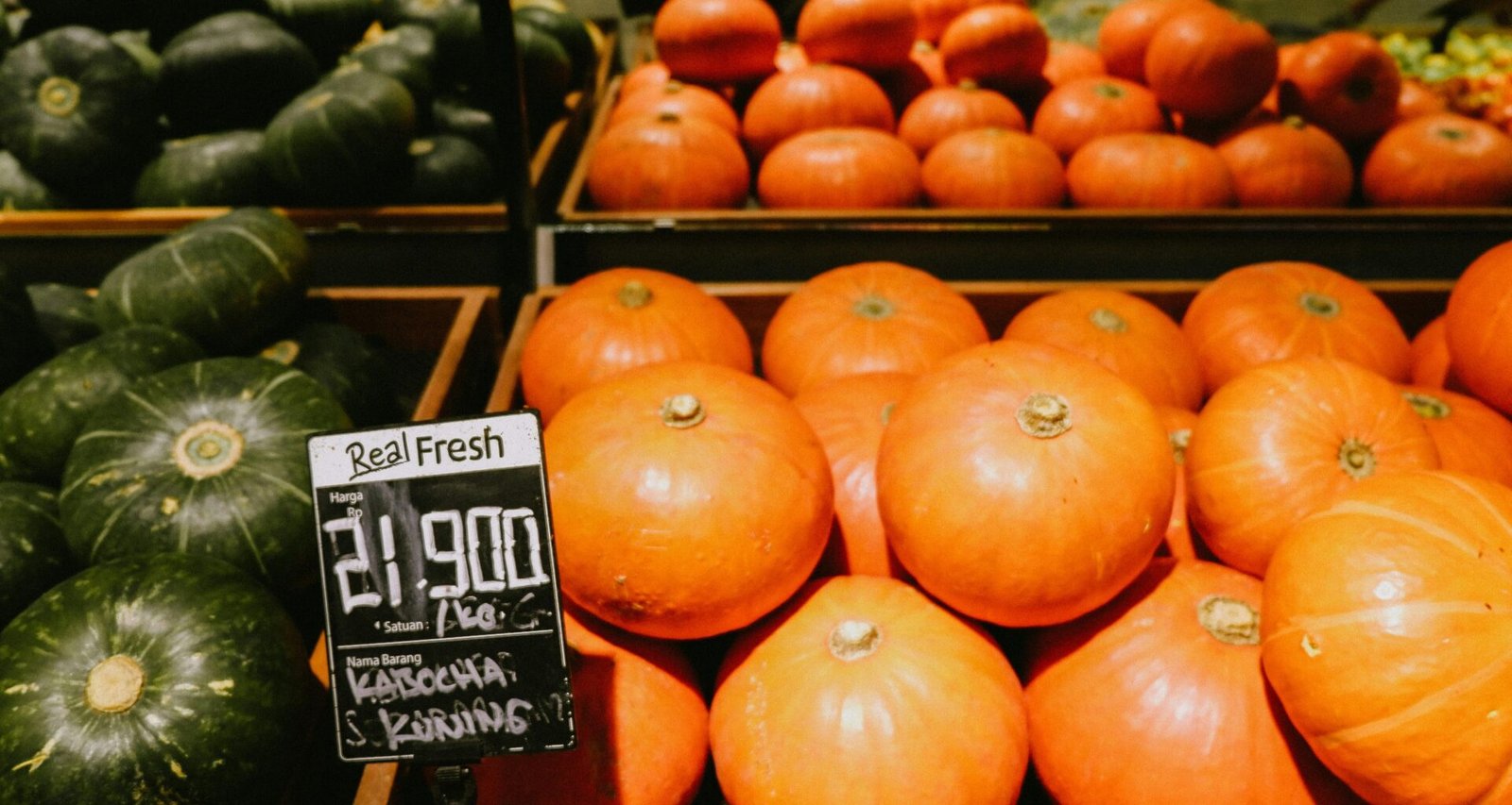 Mehrere orangefarbene Kürbisse liegen auf einer braunen Holzkiste, arrangiert für eine herbstliche Fotografie.