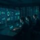 Hochmodernes Kontrollzentrum mit transparenten Monitoren, Server-Racks und Mitarbeitern, die Daten visualisieren und kontrollieren, mit futuristischem Ambiente in Blau- und Grüntönen.