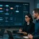 Modernes Büro mit großem Bildschirm, der Datenfluss-Visualisierung, API-Endpoints und Echtzeit-Datenströme zeigt, Fachleute beobachten aufmerksam die Darstellung.