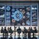 Professionelle Diskussion in einem modernen Konferenzraum über KI-Regulierung mit Digitalanzeigen, Diagrammen und internationalen Vergleichsgrafiken, unter Beteiligung diverser Fachleute.