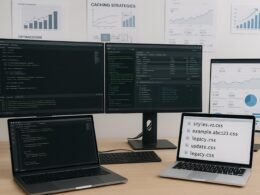 Moderner Arbeitsplatz eines Entwicklers mit Monitoren, Code-Editoren und Whiteboards, die Strategien für Asset-Versionierung und Caching zeigen.