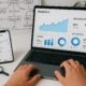 Laptop mit Analytics-Dashboard, Smartphone mit Instagram-Statistiken, Whiteboard mit SEO-Diagrammen, Tools wie Lupe, Stoppuhr und Cloud-Symbol im modernen digitalen Arbeitsplatz