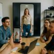 Junges Team in modernem Büro mit Smartphone, hochauflösendem Bildschirm und kreativen Whiteboards bei Videoproduktion