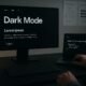 Moderner Arbeitsplatz mit Dark Mode Webseite, CSS-Code auf Laptop, technische Diagramme an der Wand, fotografiert von Tobias Hager, 404 Magazine.