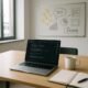Modernes, sachliches Büro mit Laptop, Notizbuch, Kaffee und Pinnwand mit Sticky Notes und SEO-Diagrammen, Tageslicht durch große Fenster, professionelle Arbeitsumgebung.