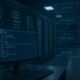Moderner Serverraum mit blauen und grünen Beleuchtungen, Monitor mit Code und schematischen Datenflussübersichten