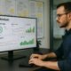 Person arbeitet in einem modernen Büro an einem Computer mit SEO-Analyse-Daten auf dem Bildschirm, im Hintergrund Whiteboards und Post-it-Notizen mit technischen Notizen