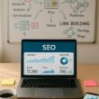 Moderner Arbeitsplatz mit Laptop, Notizen, Kaffee, Smartphone und Whiteboard mit SEO-Diagrammen, highlighting digitales Marketing und SEO-Strategien.