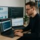 Professioneller männlicher Bloggger sitzend an modernem Schreibtisch mit mehreren Monitoren, die SEO-Daten, Code und Website-Performance anzeigen, in minimalistischer Büroumgebung